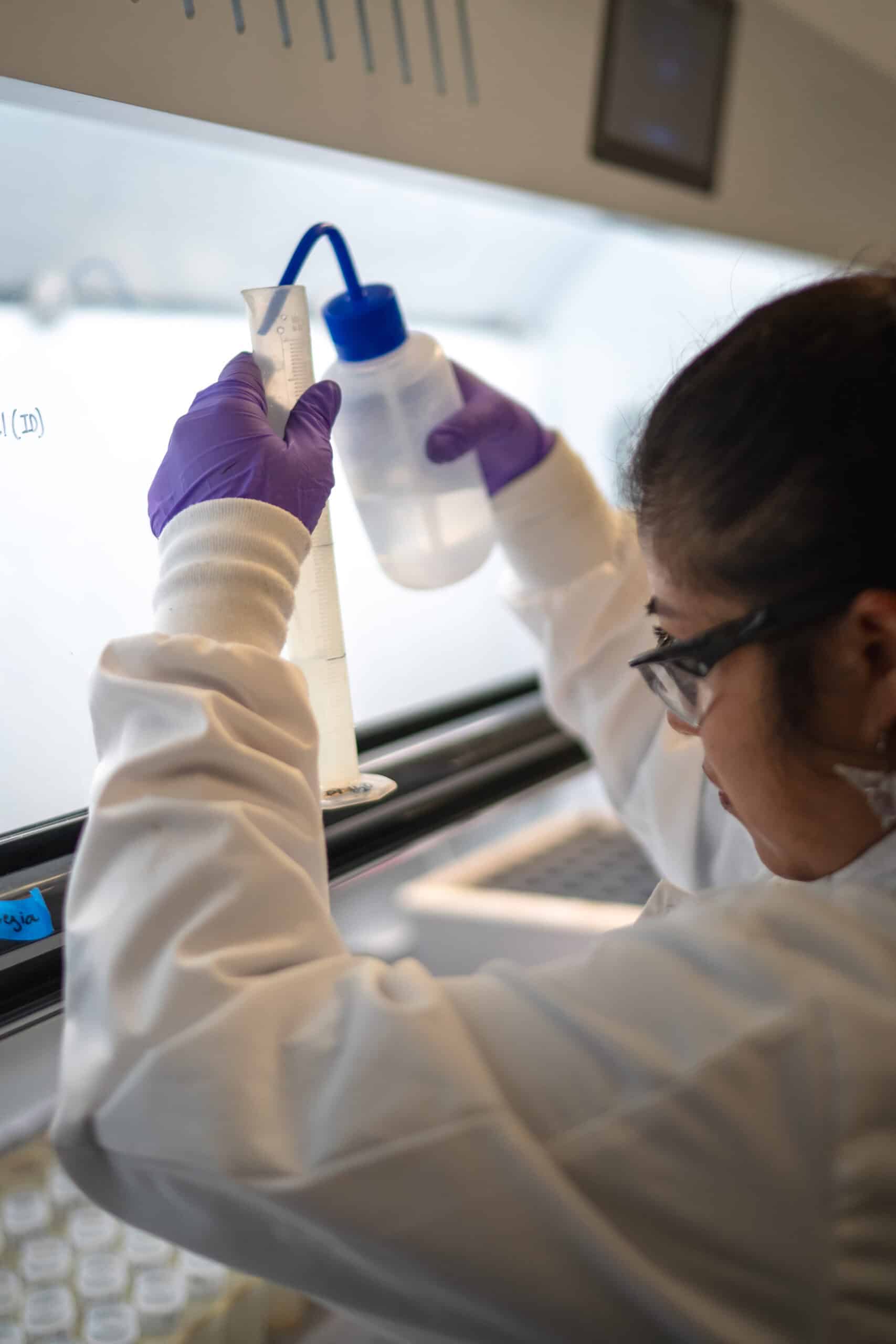 Chemist filling a sample bottle under a lab fume hood